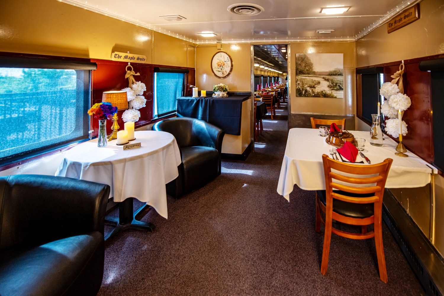 Elegant train dining car with tables, flowers, candles, and cozy armchairs.
