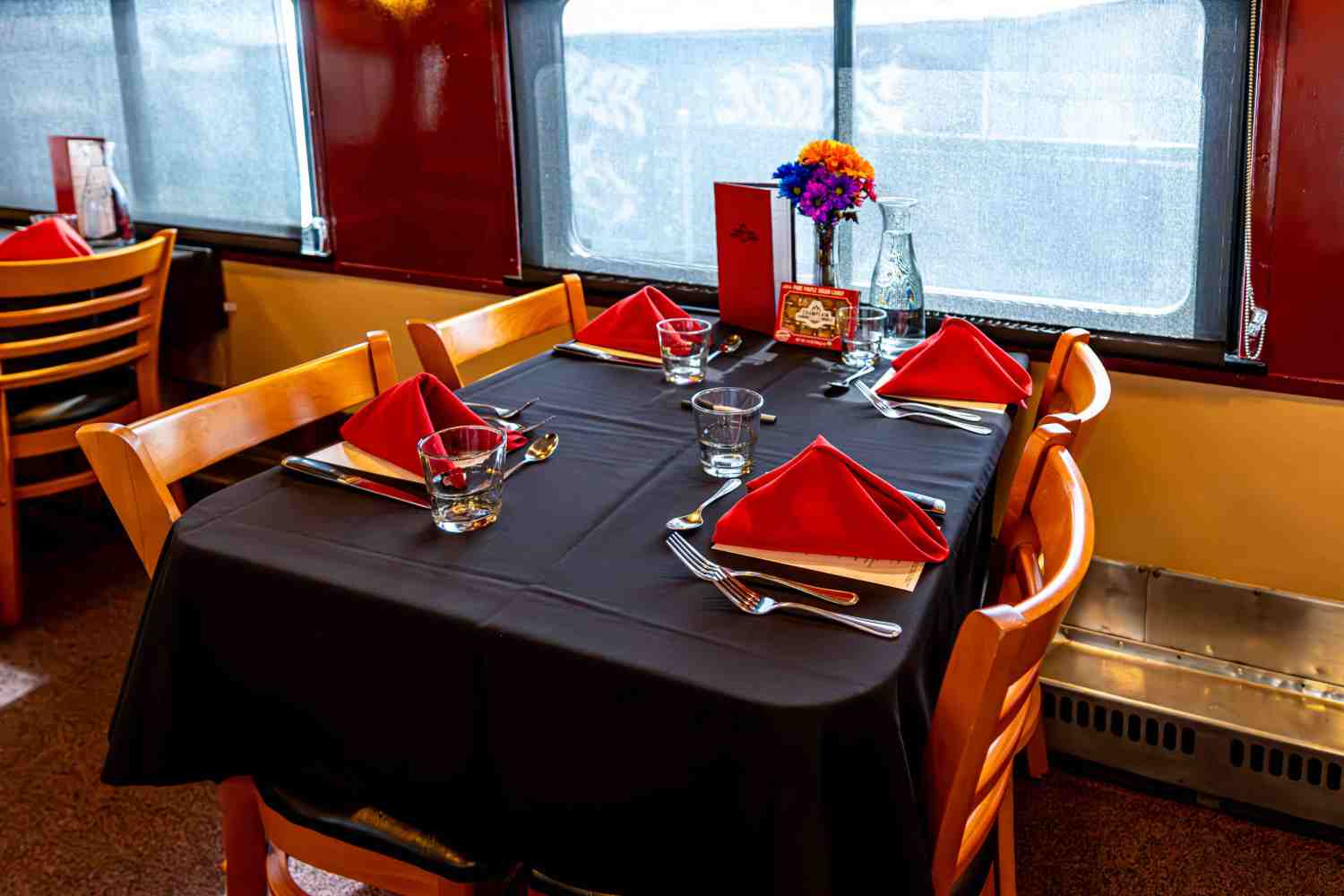 Restaurant table with red napkins and flowers, elegantly set for four people.