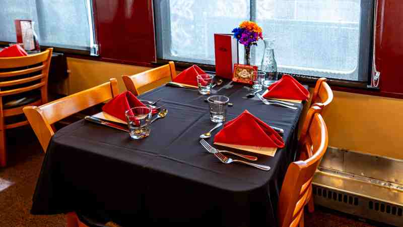 Restaurant table with red napkins and flowers, elegantly set for four people.