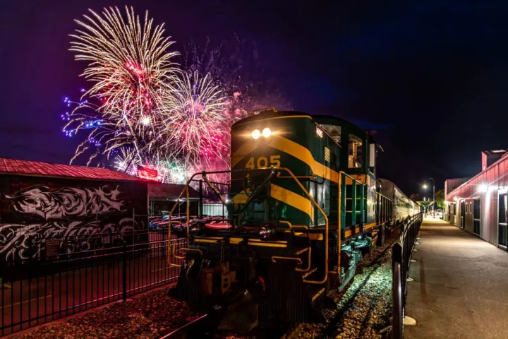 A train at night with colorful fireworks in the sky above.