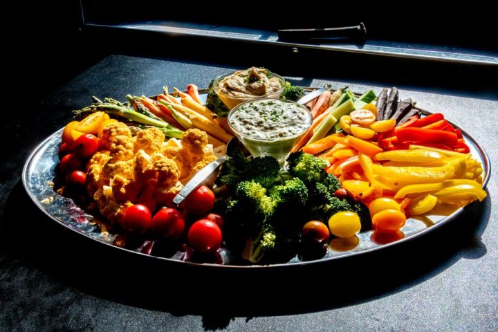 Colorful vegetable tray with assorted dips, featuring peppers, broccoli, carrots, tomatoes, and cauliflower.