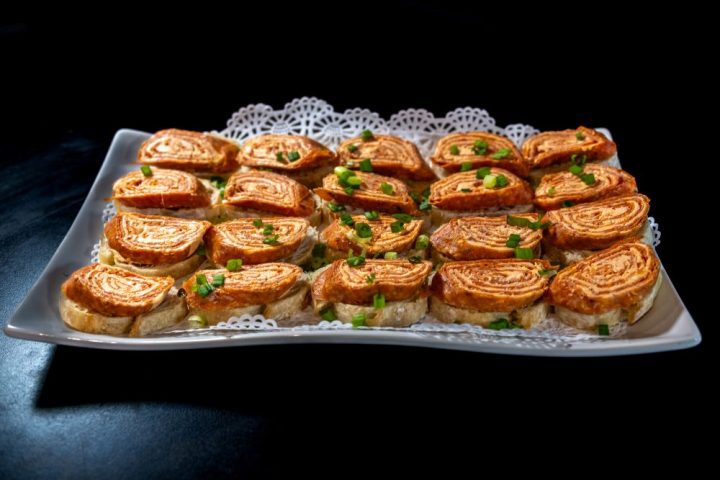 Plate of rolled omelette slices garnished with green onions on doily-lined tray.