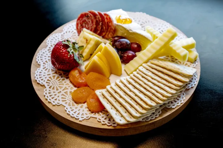 Cheese board with crackers, sliced meats, cheeses, dried apricots, strawberries, and grapes on a doily.