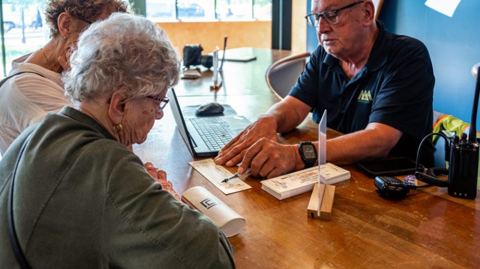 A man assisting two women with paperwork at a wooden table in an office setting.