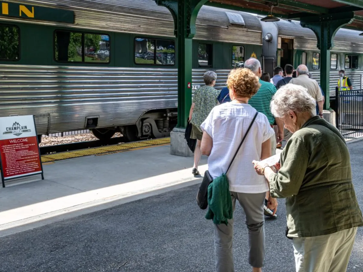 People boarding a silver train at a platform with a Champlain Valley sign.