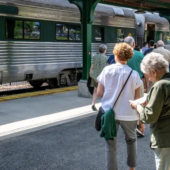 People boarding a silver train at a platform with a Champlain Valley sign.