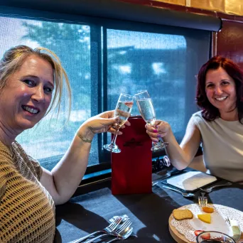 Two women at a restaurant table clinking champagne glasses and smiling.