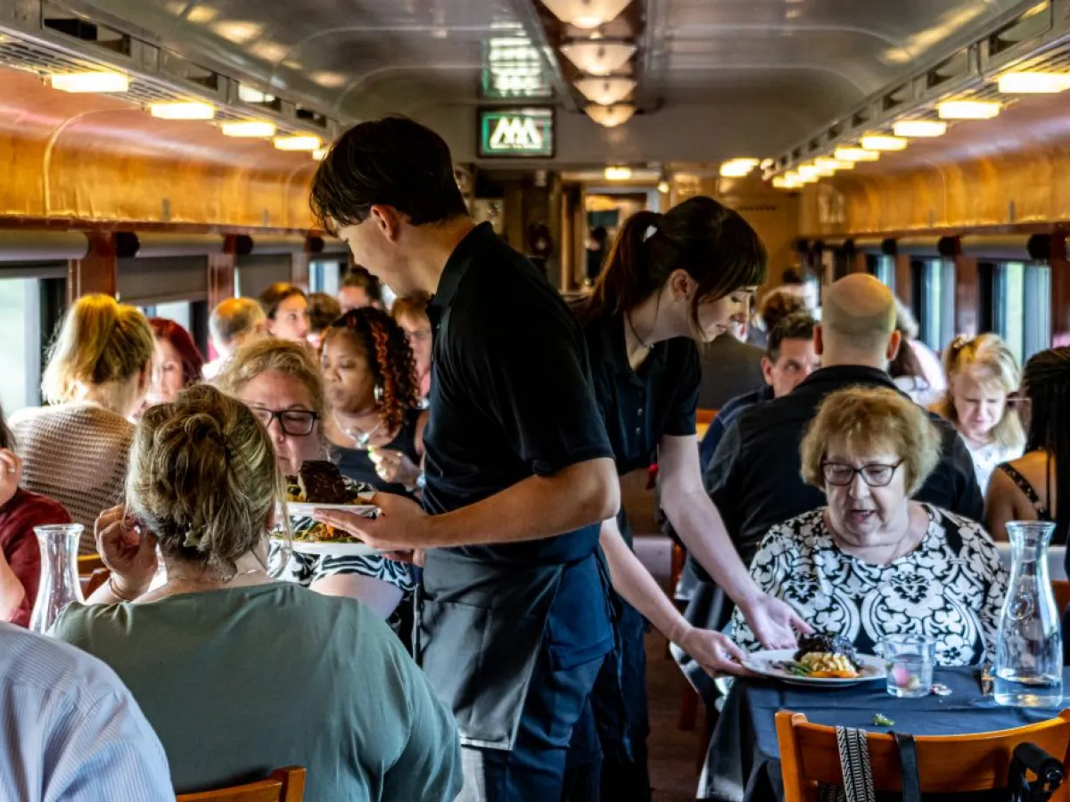 Waitstaff serving passengers on a crowded dining train car.