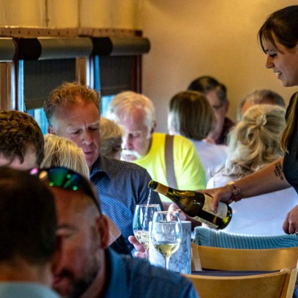 Waitress pouring wine for diners in a crowded restaurant.