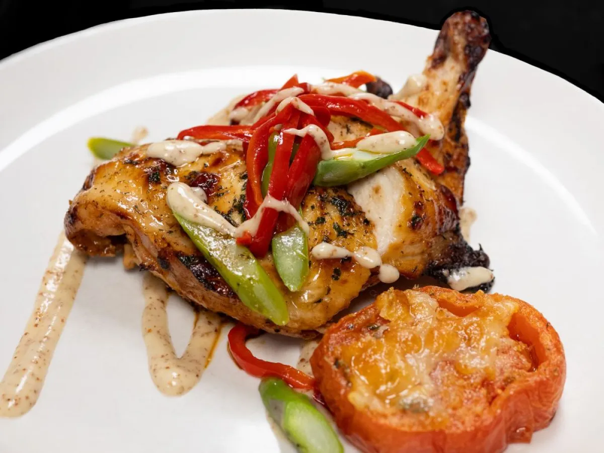 Grilled chicken with sauce, red peppers, and asparagus on a white plate with a roasted tomato.