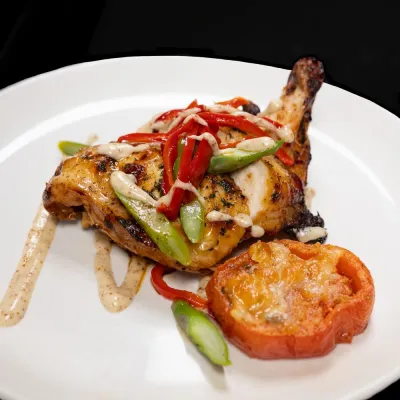 Grilled chicken with sauce, red peppers, and asparagus on a white plate with a roasted tomato.