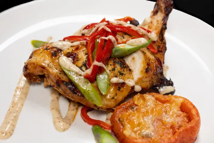 Grilled chicken with sauce, red peppers, and asparagus on a white plate with a roasted tomato.