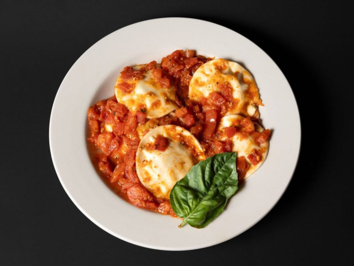 Plate of ravioli with tomato sauce and basil on a black background.