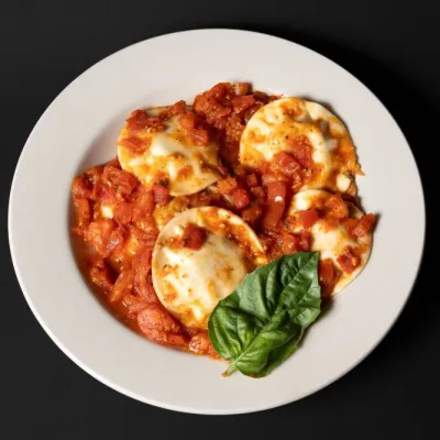 Plate of ravioli with tomato sauce and basil on a black background.