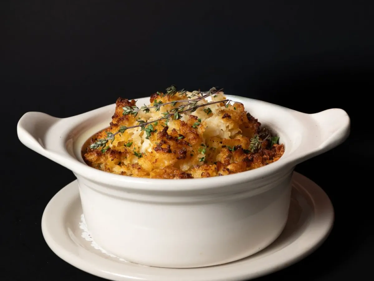 Baked dish with herbs in a white ceramic pot on a black background.
