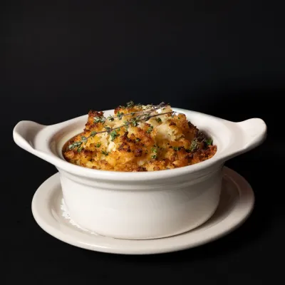Baked dish with herbs in a white ceramic pot on a black background.
