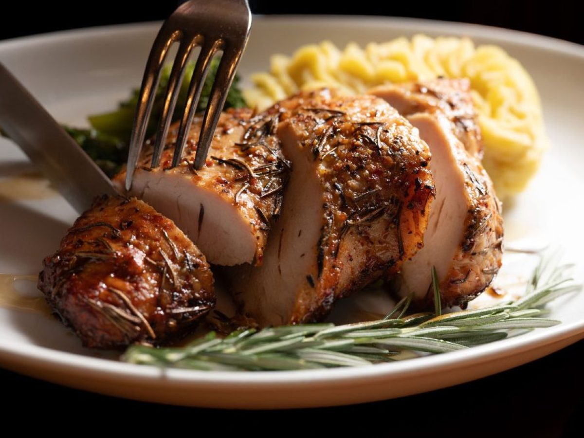 Sliced roasted chicken breast with herbs, mashed potatoes, and rosemary sprig on a plate.