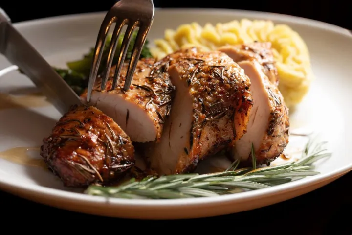 Sliced roasted chicken breast with herbs, mashed potatoes, and rosemary sprig on a plate.